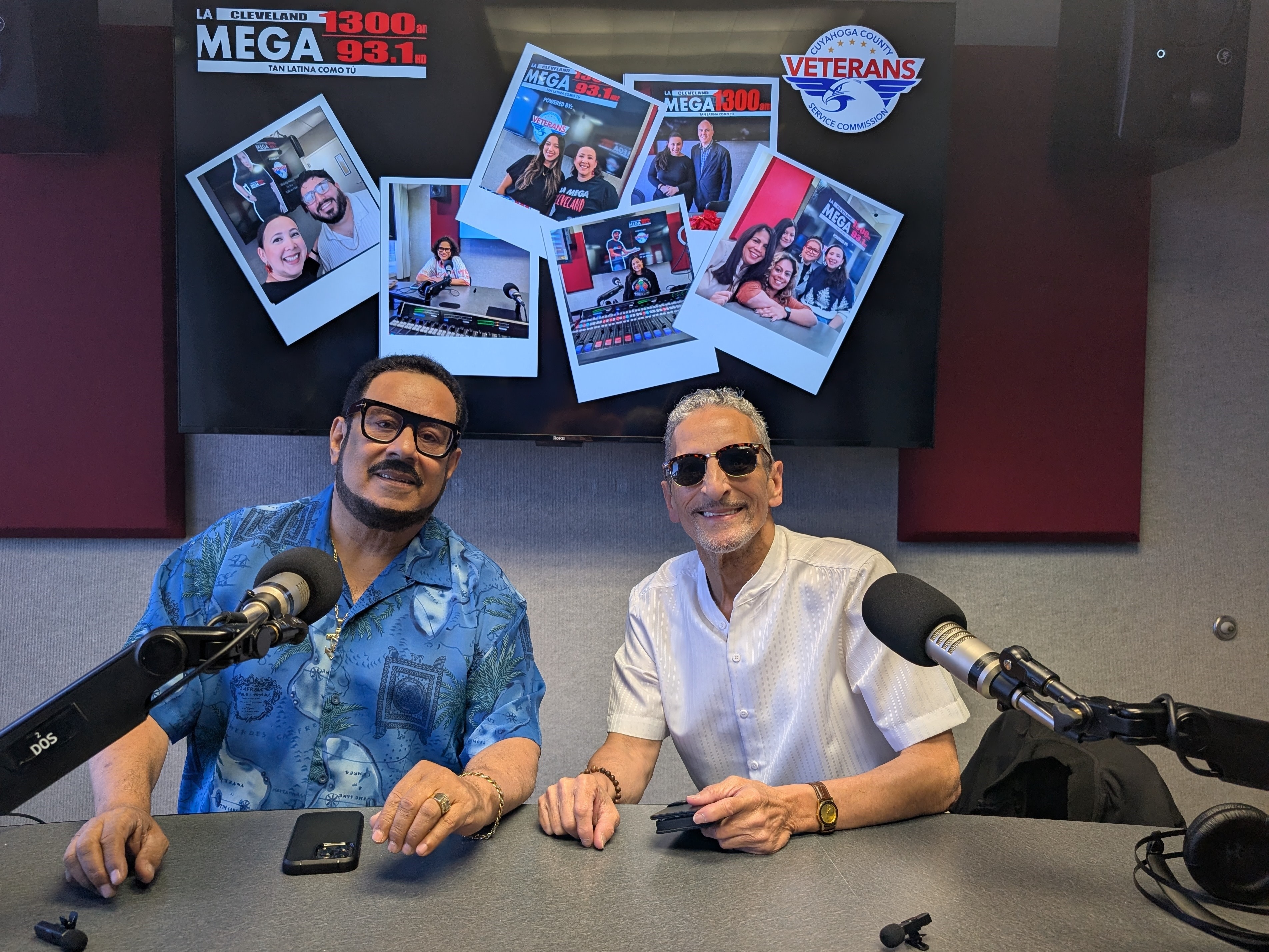 Two men sitting at a radio studio desk, surrounded by photos and branding for Mega 93.1 and Veterans radio stations.