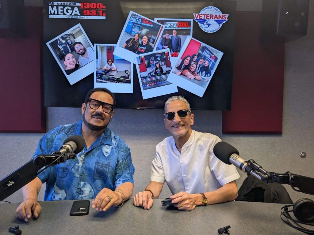 Two men sitting at a radio studio desk, surrounded by photos and branding for Mega 93.1 and Veterans radio stations.