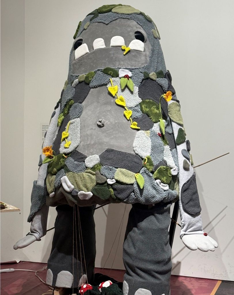 A large gray plush toy resembling the character Totoro from the Studio Ghibli films, decorated with leaves and flowers.