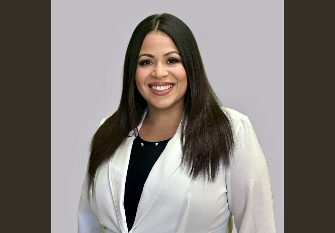 A smiling woman with long dark hair wearing a white blazer.