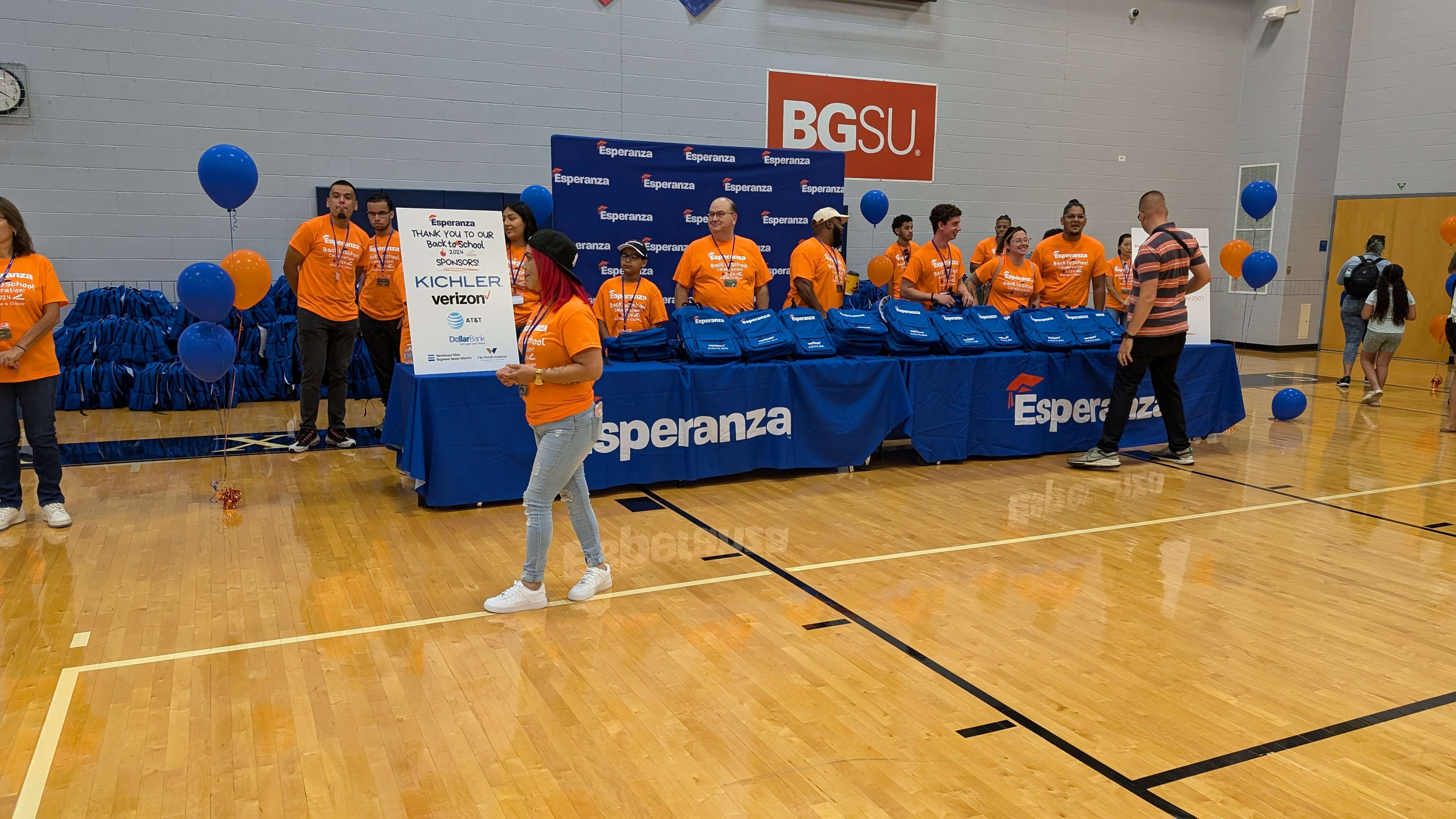 A group of people wearing orange shirts with the Esperanza logo, holding a large check and standing in front of a BGSU banner in a gymnasium.