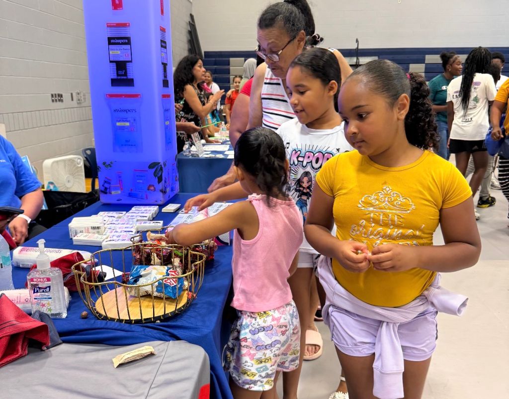A group of children and an adult examining items in a wire basket at a school event or activity.