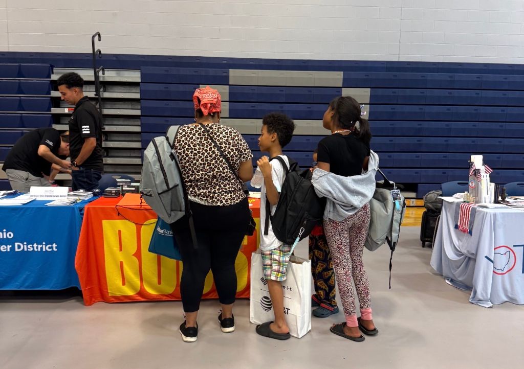 A group of people standing in front of a table with "BUS" written on it, in what appears to be a school or community setting.