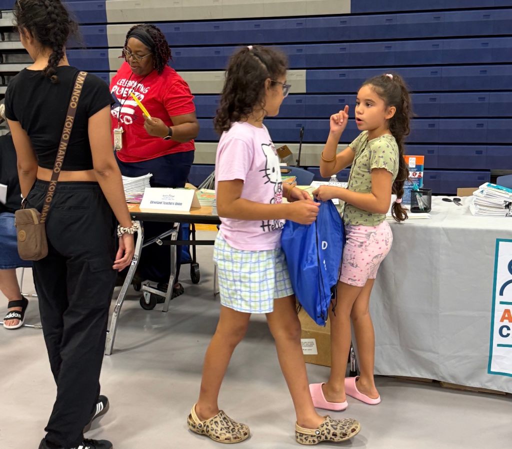 Several people, including children, standing at a table with school supplies and a "BACK TO SCHOOL" sign.