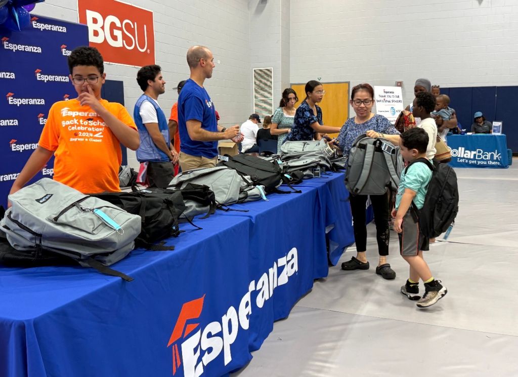 A group of people, some wearing blue shirts with "BGSU" and orange shirts with "Back to school celebration 2022", standing around a table with Esperanza and DollarBank branding.