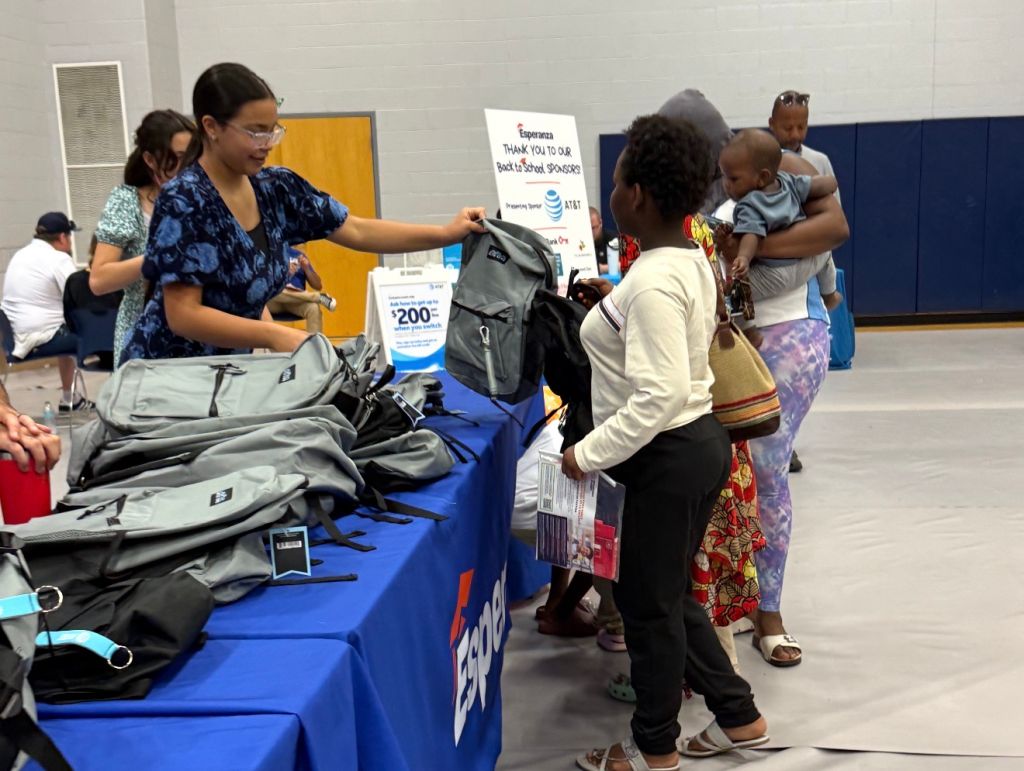 A group of people, including adults and children, at a back-to-school event. A table displays "THANK YOU TO OUR BACK TO SCHOOL SPONSORS" and AT&T branding.