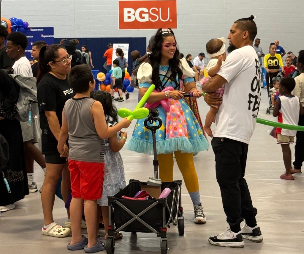 Crowded indoor event space with BGSU logo. People of various ages, including children, interacting with a costumed character holding a balloon.