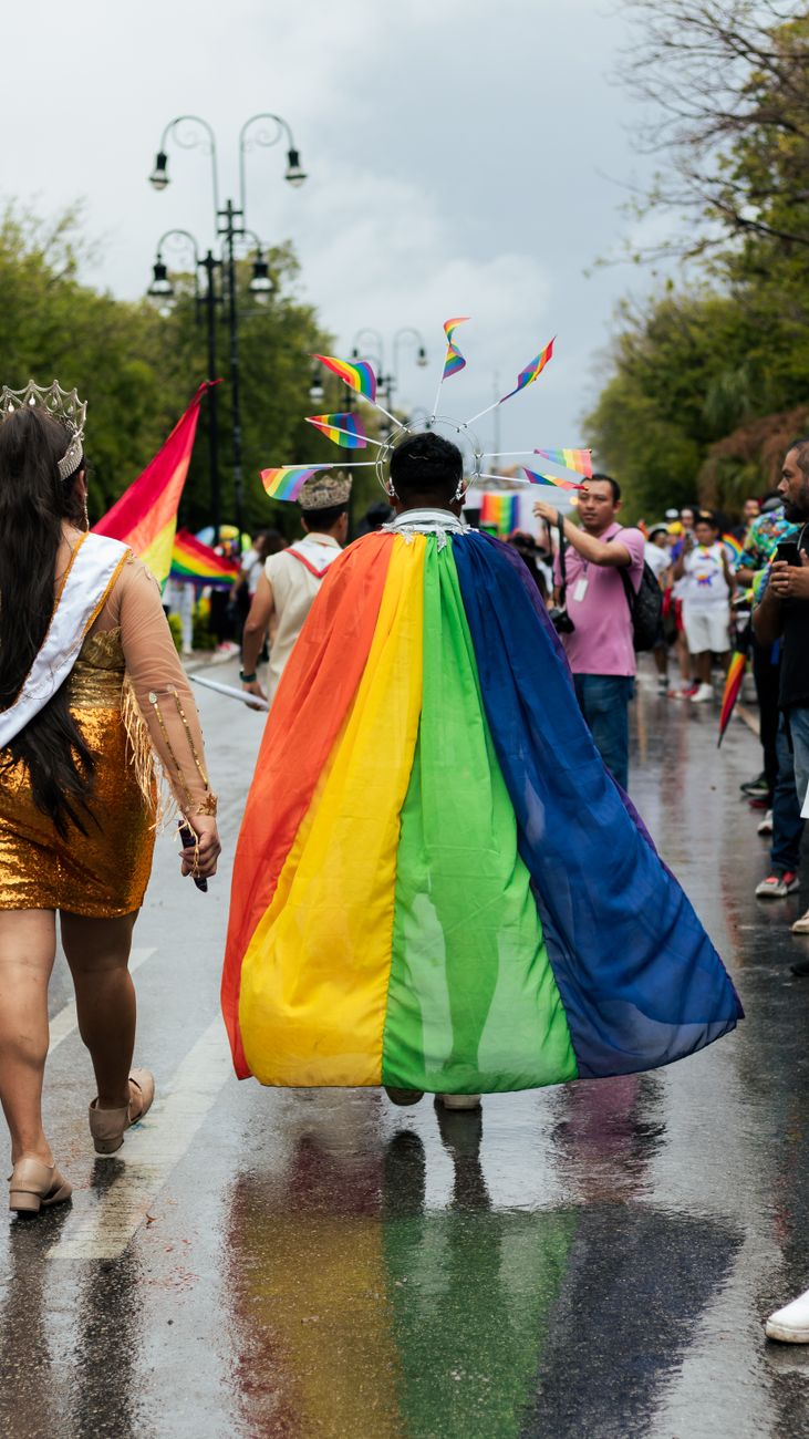 person in cape and halo crown with lgbt flags at the pride parade