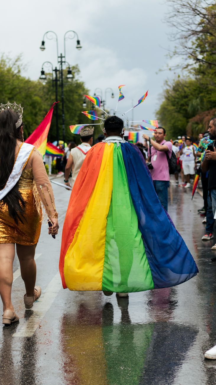 person in cape and halo crown with lgbt flags at the pride parade